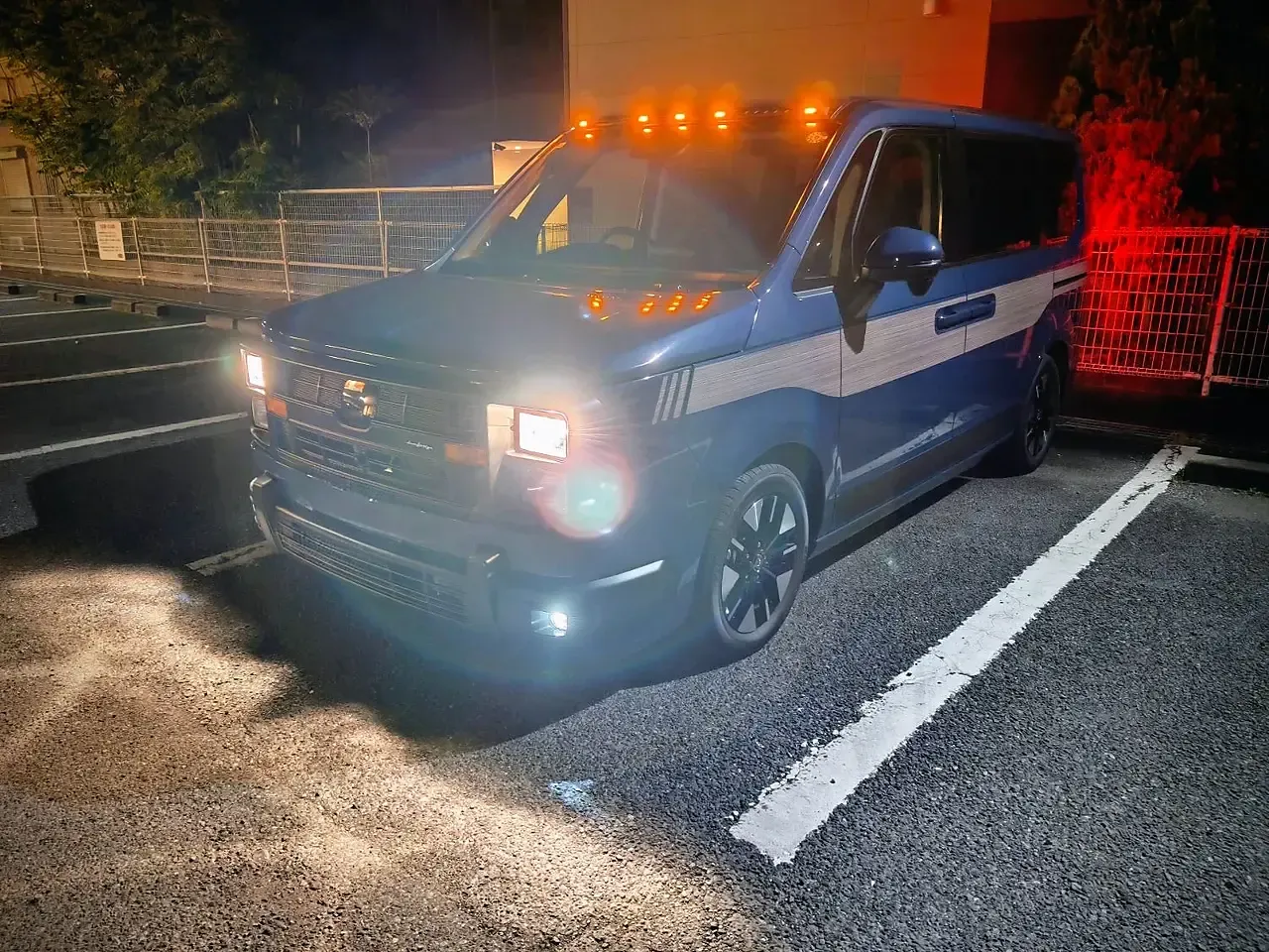 夜の駐車場でのフロントビュー。ヘッドライトとマーカーランプが点灯している
